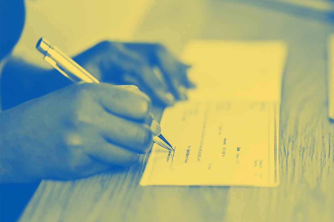 A yellow tinted image on someone signing a check on a desk.