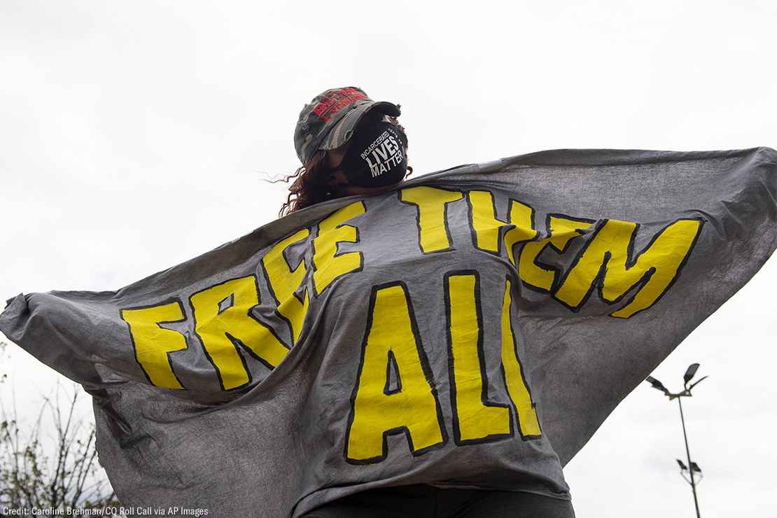 A masked protester is seen wrapped in a sign that says FREE THEM ALL