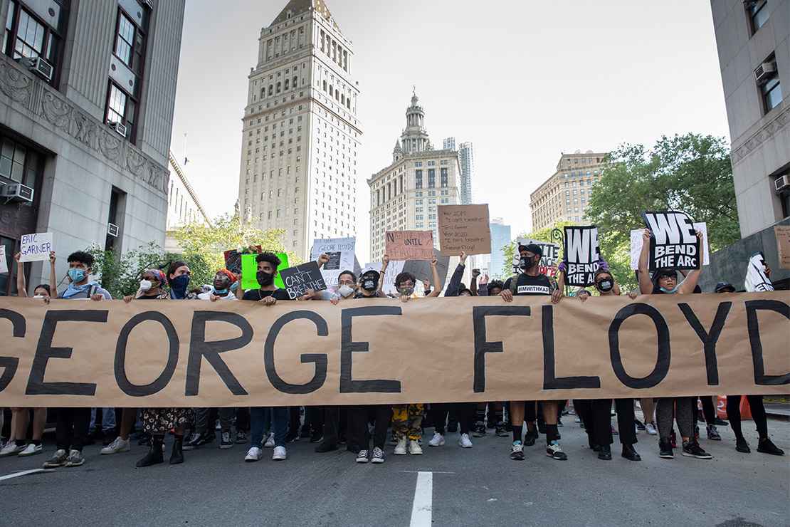 Black Lives Matter demonstrators marching with a large banner with George Floyd's name.