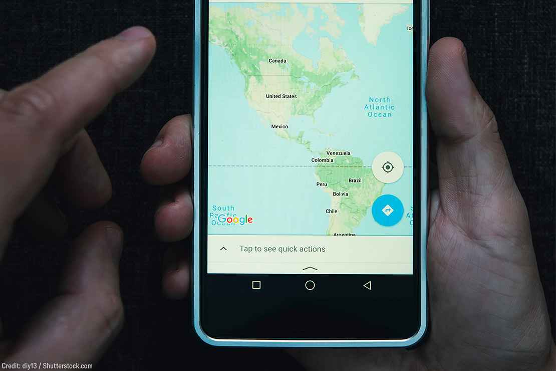 One hand holding a cell phone while the other hovers with index finger extended over a smart phone showing a map of North and South America.