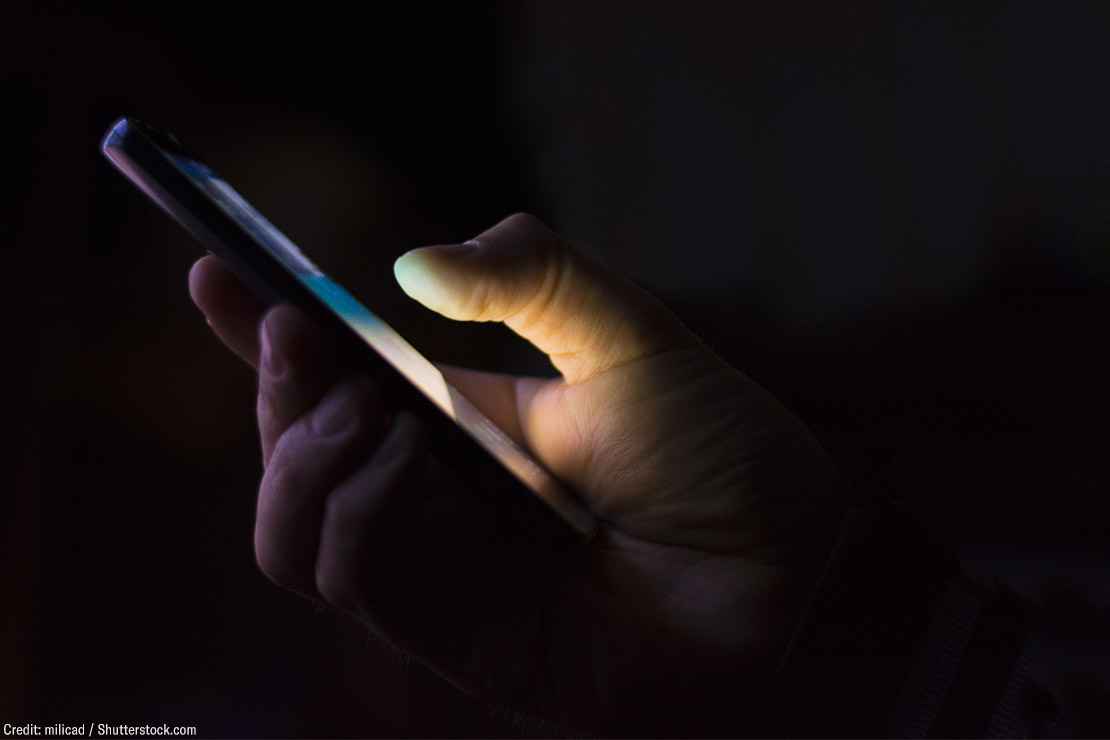 A hand holding a smart phone shrouded in darkness.