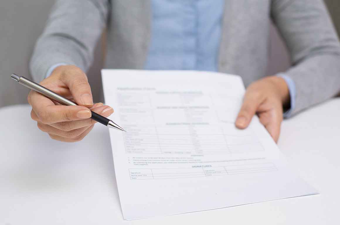 Image of a hand offering a pen to sign a document