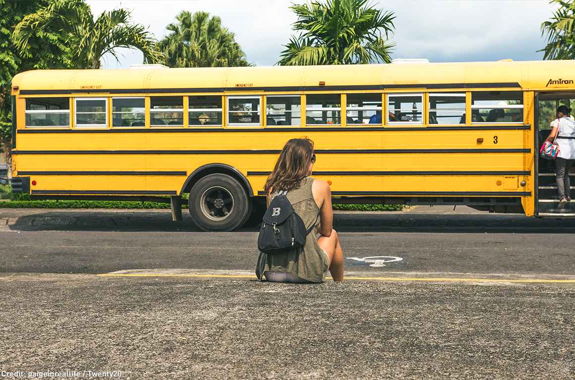 Girl sitting outside with school bus