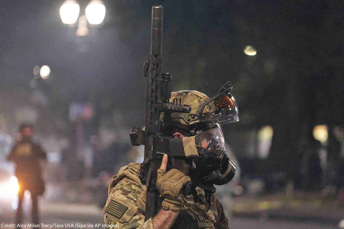 An ICE agent holds his weapon in the air as federal officers clear Main Street in Portland, Ore., on July 26, 2020.